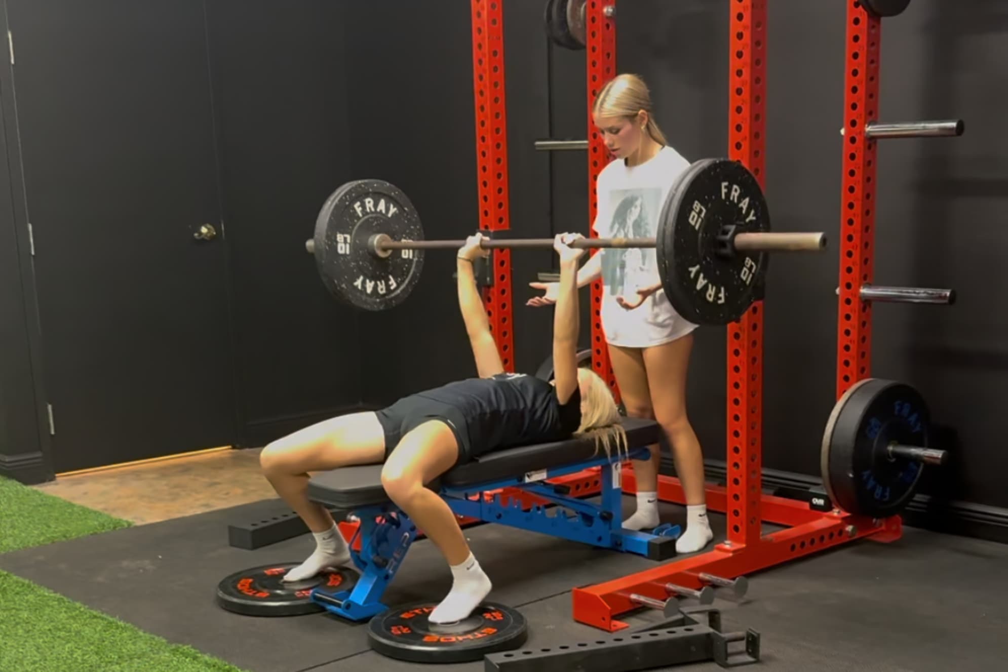 Athlete bench pressing while a teammate spots her
