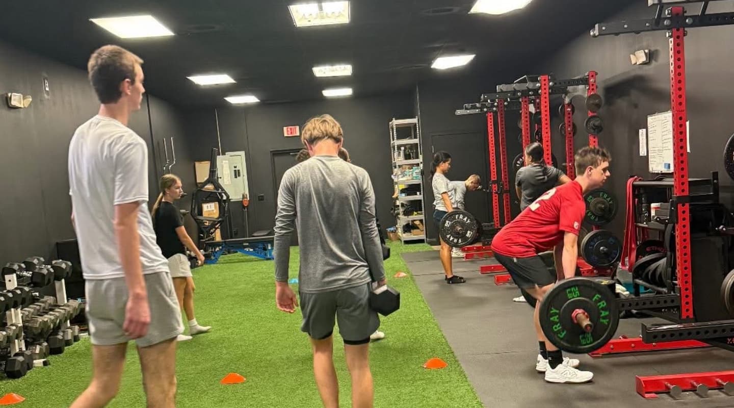 Athletes doing dumbbell carries and barbell deadlifts at the racks